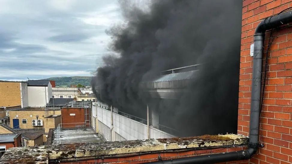 The car park next to Regent Arcade Shopping Centre. Thick black smoke can be seen coming from the multi-storey. 