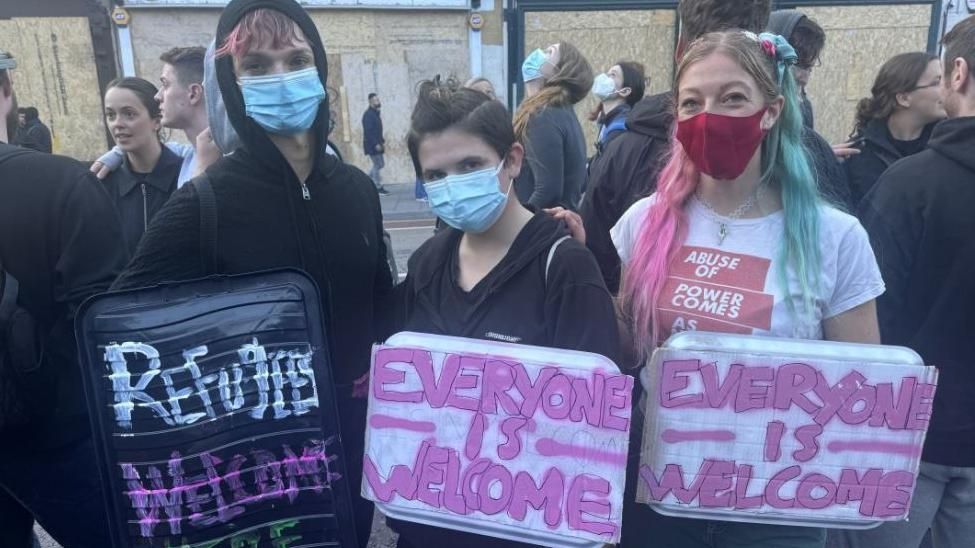 Three people at a rally in Bristol. One holds a sign that says 'Refugees Welcome', the other two have signs that say 'Everyone is Welcome'