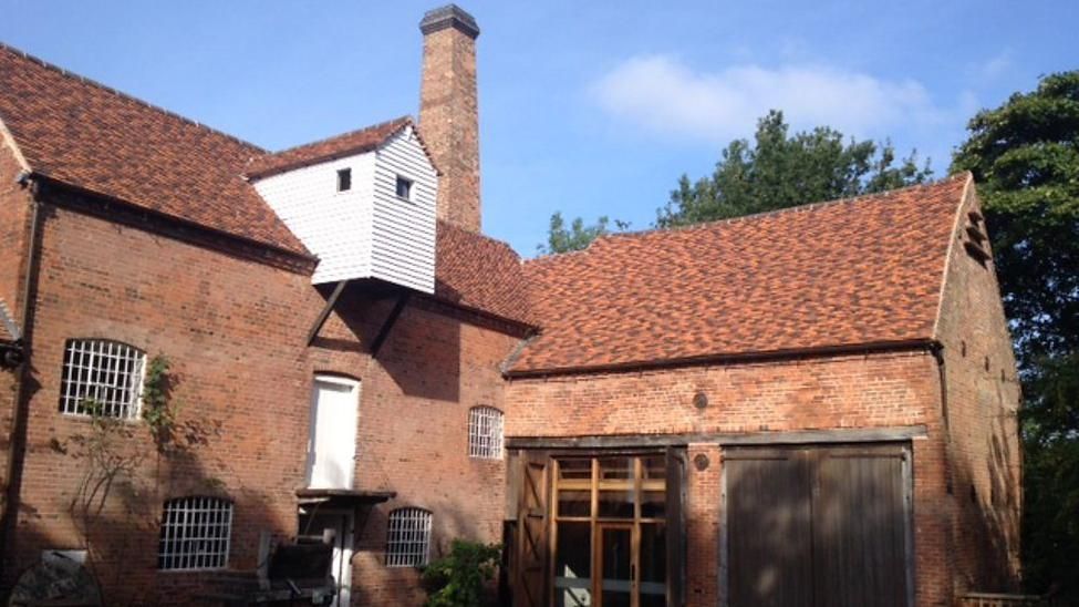An image of the exterior red brick building with chimney, brown barn doors and lead detailed windows which make up Sarehole Mill 