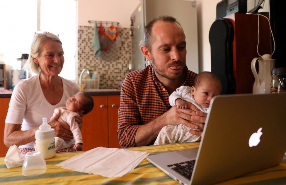 Phillip Lühl holds one of his twin daughters as his mother Frauke looks on while he speaks to his Mexican husband Guillermo Delgado via Zoom meeting in Johannesburg.