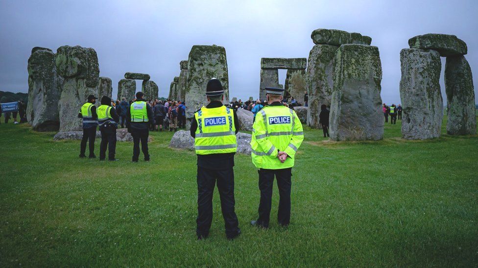 Police watch crowds celebrate during Summer Solstice at Stonehenge, where some people jumped over the fence to enter the stone-circle to watch the sun rise at dawn of the longest day in the UK. The stones have been officially closed for the celebrations, which see huge crowds inside the circle, due to the coronavirus lockdown extension.