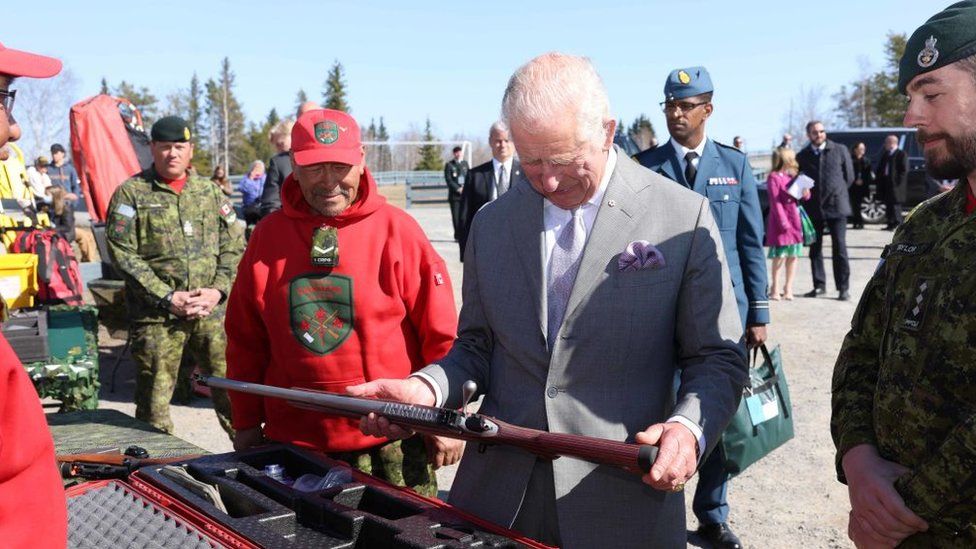 The prince examines a rifle in his hands in the presence of Rangers and other military personnel