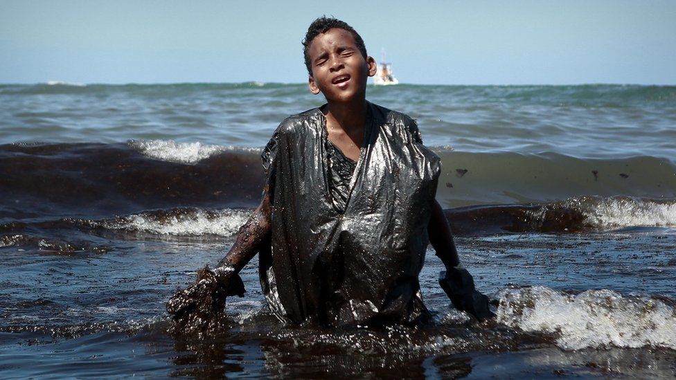 Boy walks out of the sea covered in oil