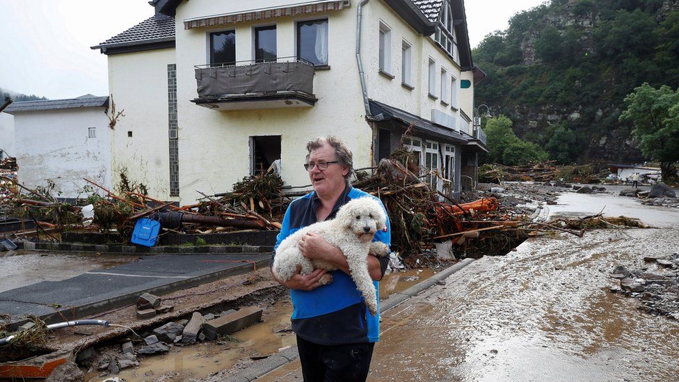 A man carries a dog next to debris brought by the flood