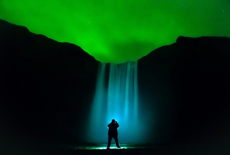 A waterfall is illuminated under the aurora lit sky