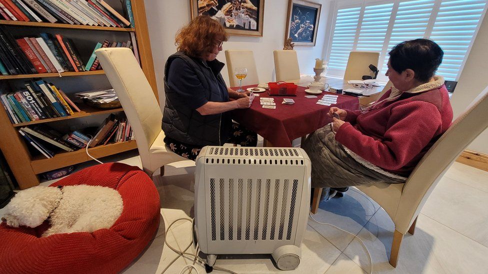 Two women play cards by an electric heater