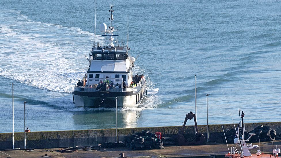 Migrants picked up at sea while attempting to cross the English Channel, arrive at the port on UK Border Force cutter 'BF Defender' (L) in Dover, southeast England, on January 2, 2023