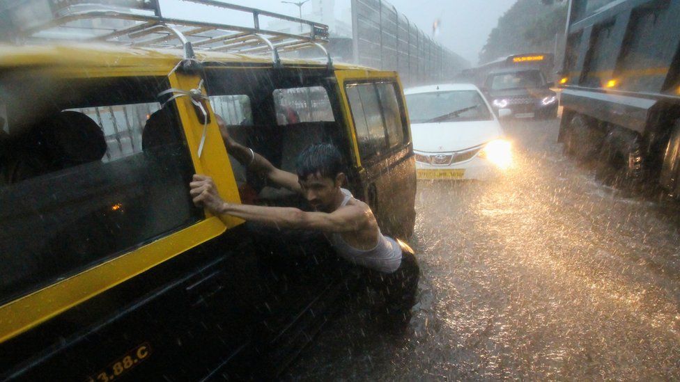 A man pushes a taxi through a waterlogged street during heavy rains in Mumbai, India on 01 July 2019
