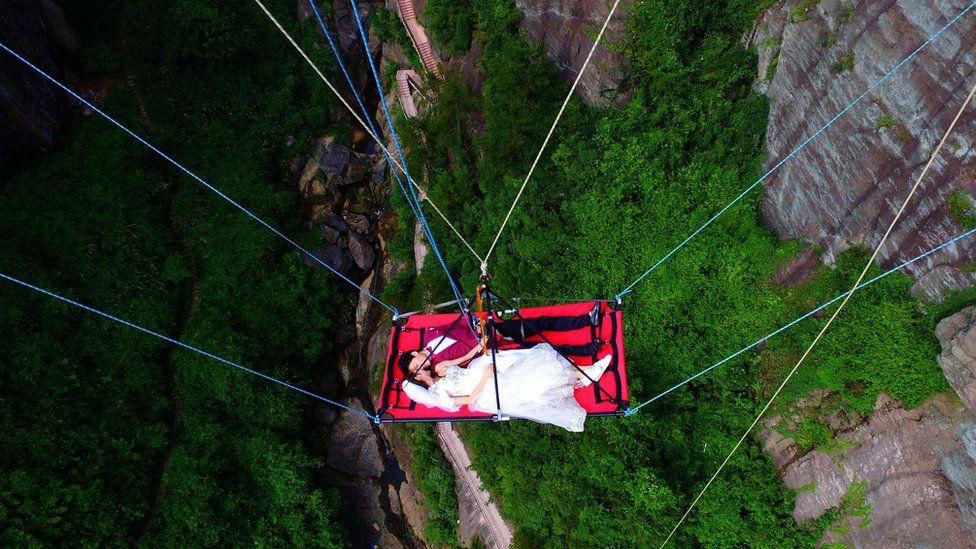 A newly married couple is lowered from a glass bridge during a promotional event in Pingjiang, Hunan province