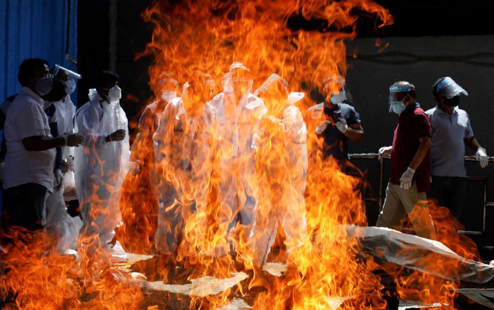 People wearing personal protective equipment look on as a man is cremated in New Delhi, India
