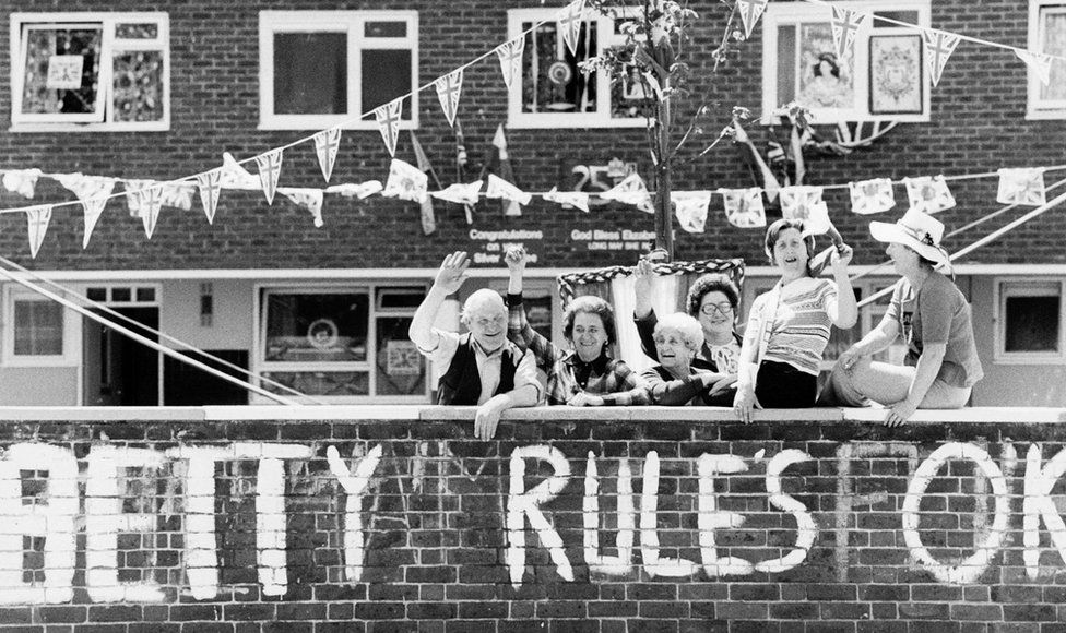 A group of Fulham residents show their support for Queen Elizabeth II's twenty-fifth year of her reign by waving enthusiastically under strings of banners