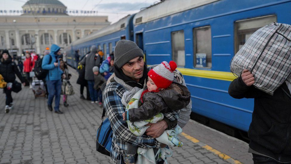 A man carries a child as he boards a train at a railway station in Odessa on 9 March 2022.