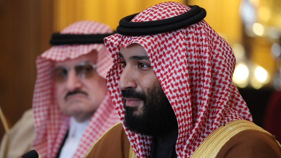 Prince Mohammed bin Salman pictured sitting at a table, smiling at something out of frame