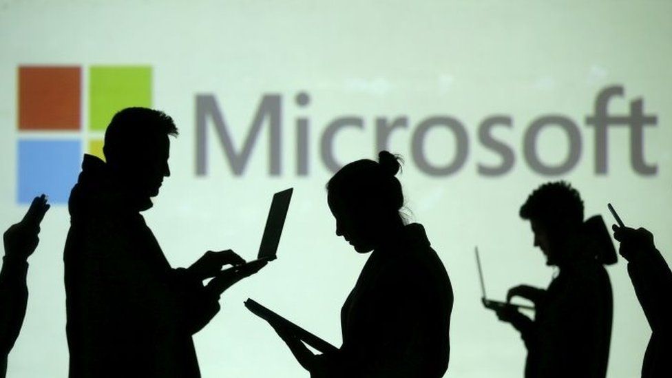 Силуэты людей, использующих электронику перед логотипом Microsoft