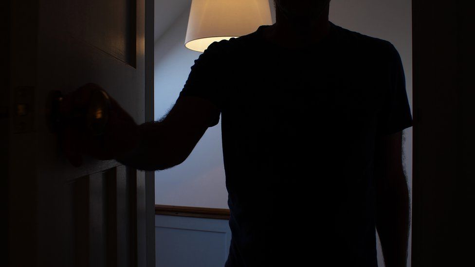 Silhouette of a man opening a door to a dark room