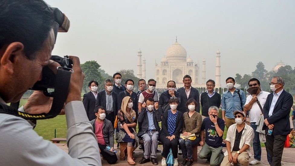 Tourists wear masks as they pose for photographs during their visit of the Taj Mahal