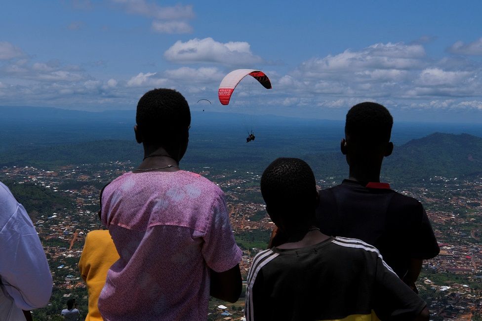 People watch as paragliders glide with passengers during the annual Easter paragliding festival in Kwahu-Atibie, Ghana.