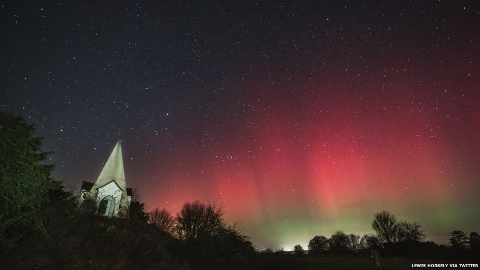 Aurora made up of dark green and red with a church spire visible in foreground
