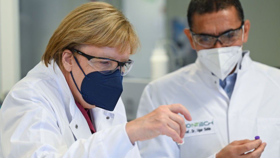 Ugur Sahin, themeluesi dhe drejtori ekzekutiv i kompanisë bioteknologjike BioNTech i tregon kancelares gjermane Angela Merkel ampula marramendëse të vaksinës BioNTech/Pfizer COVID-19 gjatë vizitës së saj në Uzinën e Prodhimit të Vaksinave BioNTech më 19 gusht 2021 në Marburg, Gjermani.