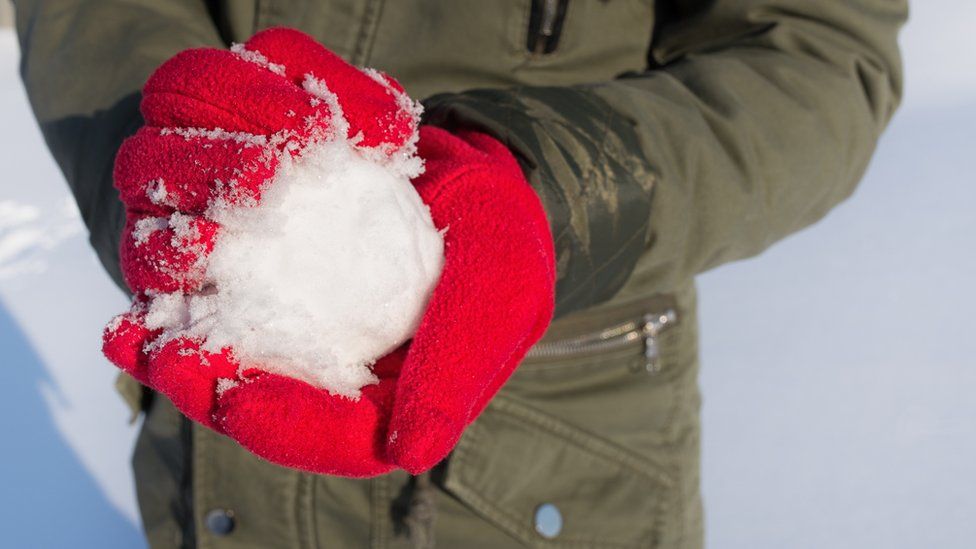 A person, wearing red gloves, making a snowball