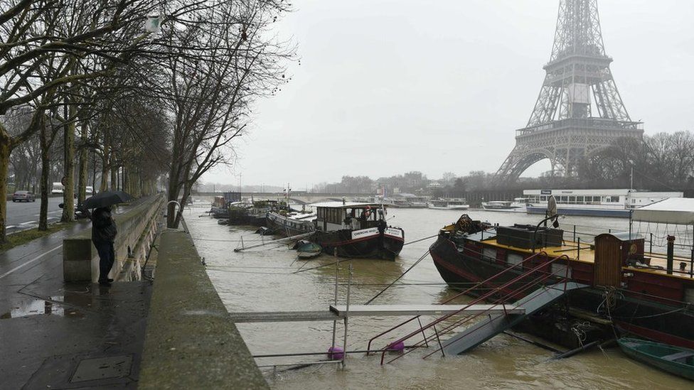 A man under an umbrella looks at the flooded river Seine level in front of the Eiffel tower in Paris on 23 January 2018