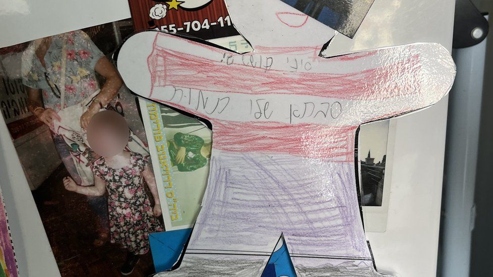 Image on fridge shows child's drawing and photo of child with face blurred