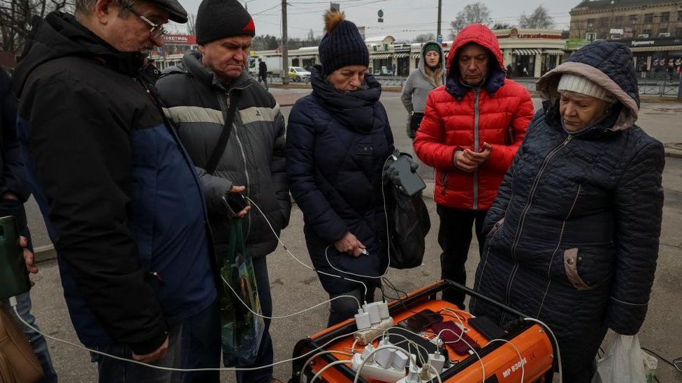 Local residents charge their phones powered by a generator at a street during a power outage after critical civil infrastructure was hit by Russian missile attacks, as Russia's invasion of Ukraine continues, in Kharkiv, Ukraine March 9, 2023