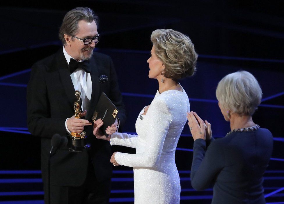 Gary Oldman onstage accepting his Oscar from Jane Fonda