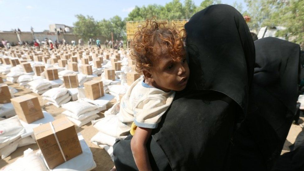 A woman carries her son as she waits for food aid at an ICRC aid distribution centre in Bajil, Yemen on 13 December 2018,