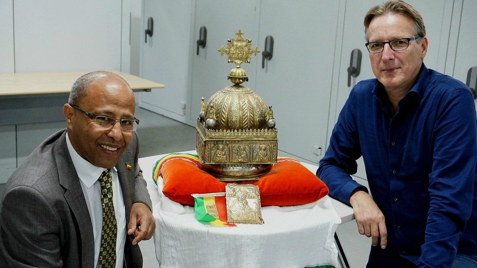 Sirak Asfaw and Arthur Brand sit next to the crown, which depicts the Holy Trinity and Christ's twelve disciples