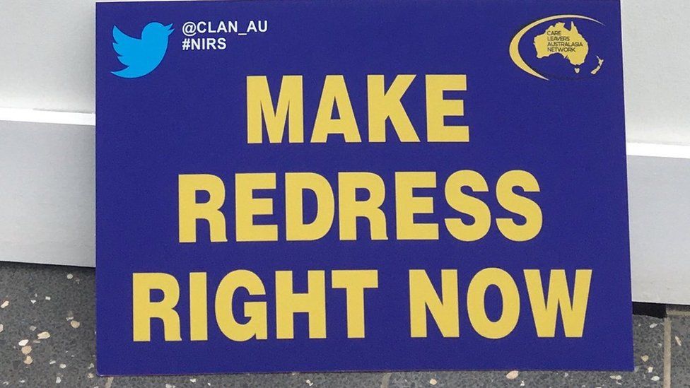 A survivor group's protest placard reads: Make redress right now