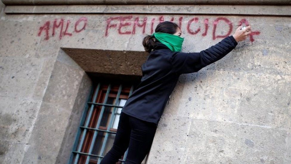A woman with a spray can daubs a slogan reading AMLO women murderer on the wall of the National Palace