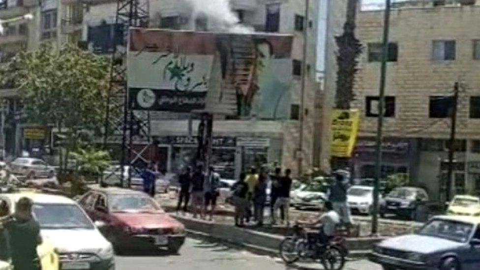 A video from Suwayda24 showing a banner featuring a photo of President Bashar al-Assad on fire in Suweida's Tishreen square
