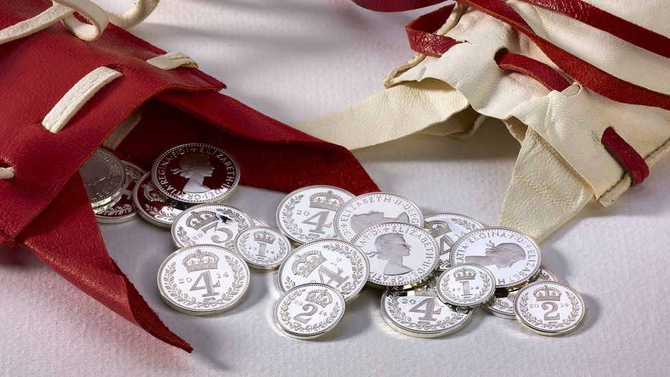 Silver Maundy coins seen spilling out of a red leather purse