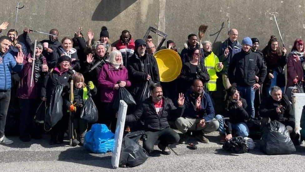 Migrants from the Bibby Stockholm and local people posing with full bin bags following a beach litter clean