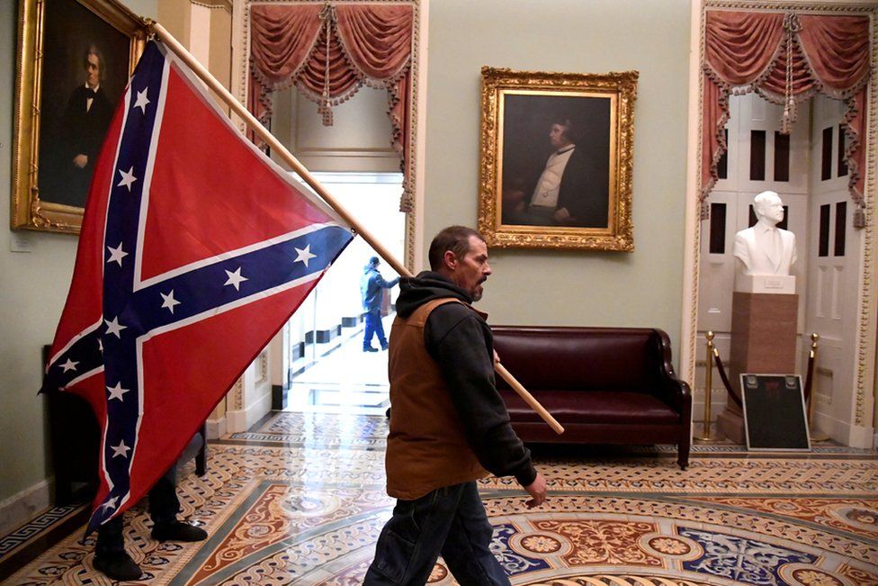 Сторонник президента Дональда Трампа несет флаг Конфедерации на втором этаже Капитолия США у входа в Сенат после нарушения системы безопасности в Вашингтоне, округ Колумбия. 6 января 2021 г.