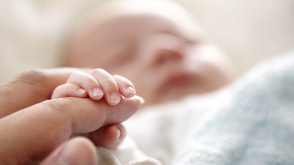 Stock image of a person holding a newborn baby's hand