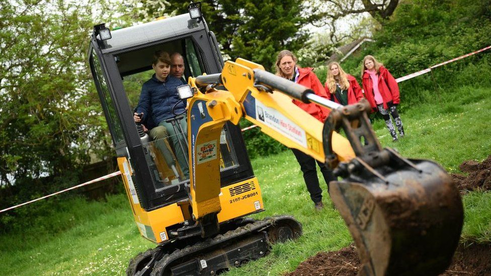Britain's Prince William, Prince of Wales is helped by Britain's Prince George of Wales (L) as he uses an excavator while taking part in the Big Help Out