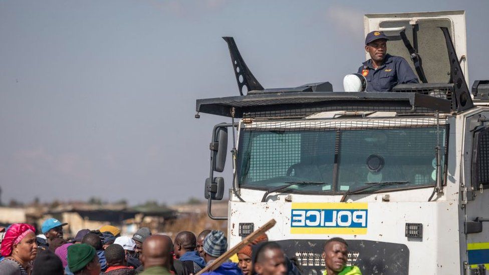 Офицер южноафриканской полицейской службы (SAPS) на вершине Nyala (бронированный автомобиль) рядом с жителями, протестующими против незаконной добычи полезных ископаемых и роста преступности в районе Кагисо, 4 августа 2022 года.