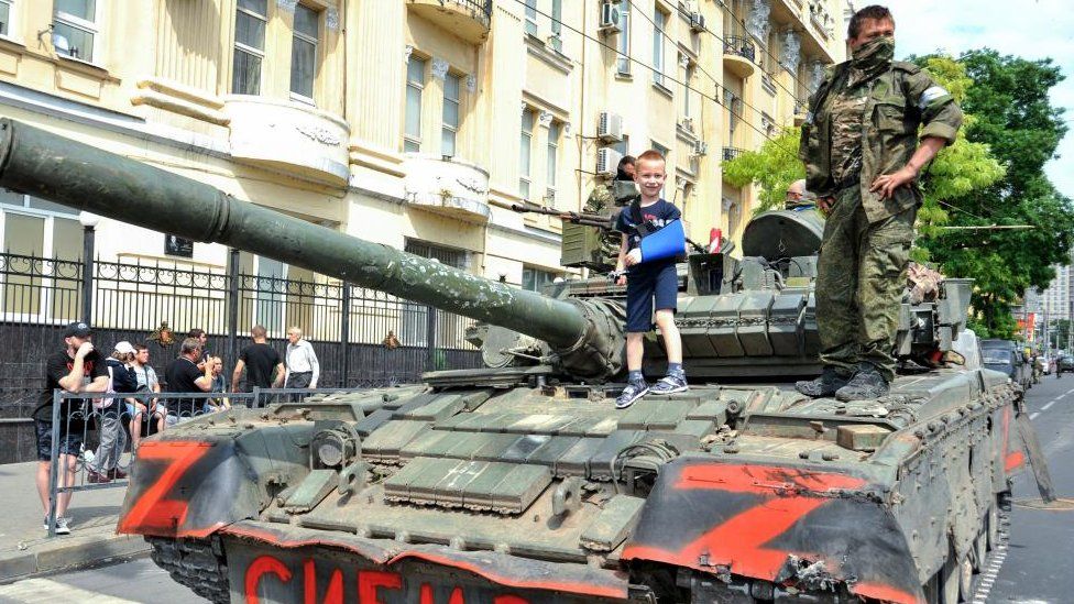 A child poses for a photo on a tank reading 'Siberia' as servicemen from private military company (PMC) Wagner Group block a street in downtown Rostov-on-Don