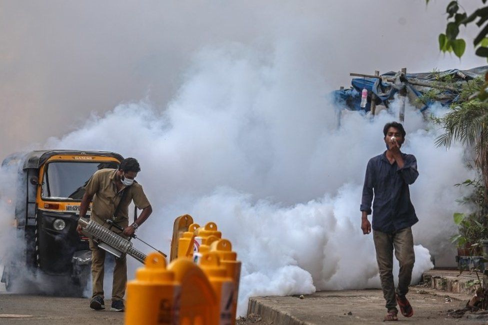 A municipal worker wearing a face mask uses a fumigation spray machine near a vaccination centre in Mumbai, India, 30 April 2021.