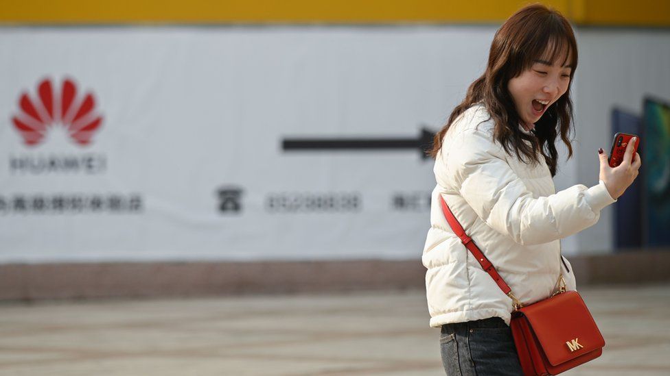 A woman laughs while using her smartphone outside a Huawei store in Beijing on January 29, 2019.