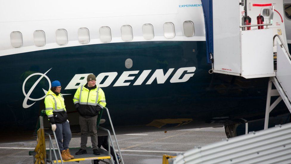 Workers standing next to a grounded Boeing 737 Max 9 aircraft
