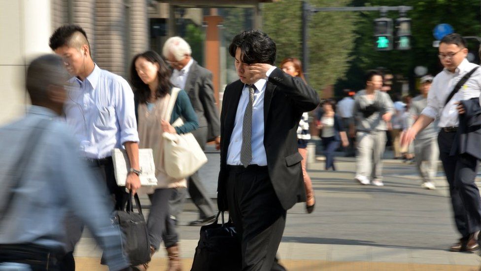A sleepy Japanese business man rubs his eyes as he walks across the road in Tokyo