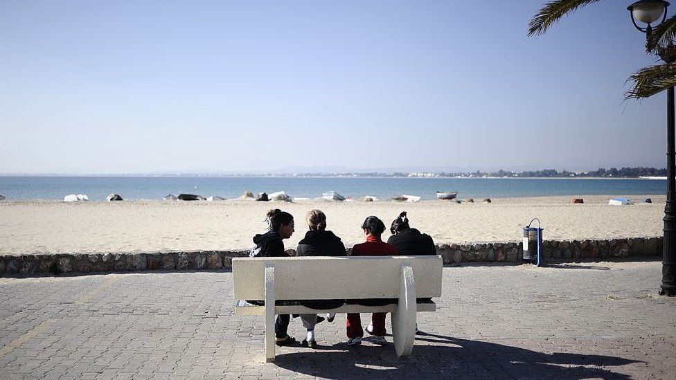 People sit on a bench facing the sea in Hammamet