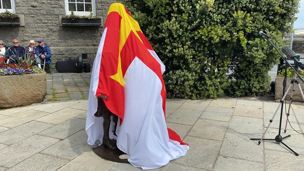 Статуя задрапирована флагом Гернси перед открытием