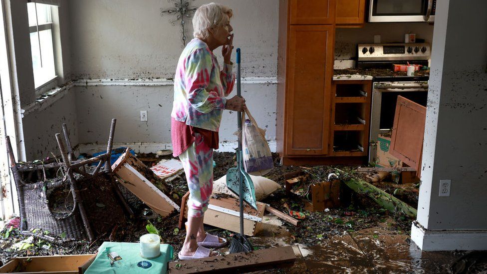 A woman stands in shock as she tries to clean her home littered with debris from the hurricane.