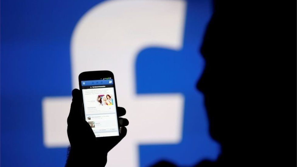 FILE PHOTO: A man is silhouetted against a video screen with a Facebook logo as he poses with a Samsung S4 smartphone in this photo illustration August 14, 2013