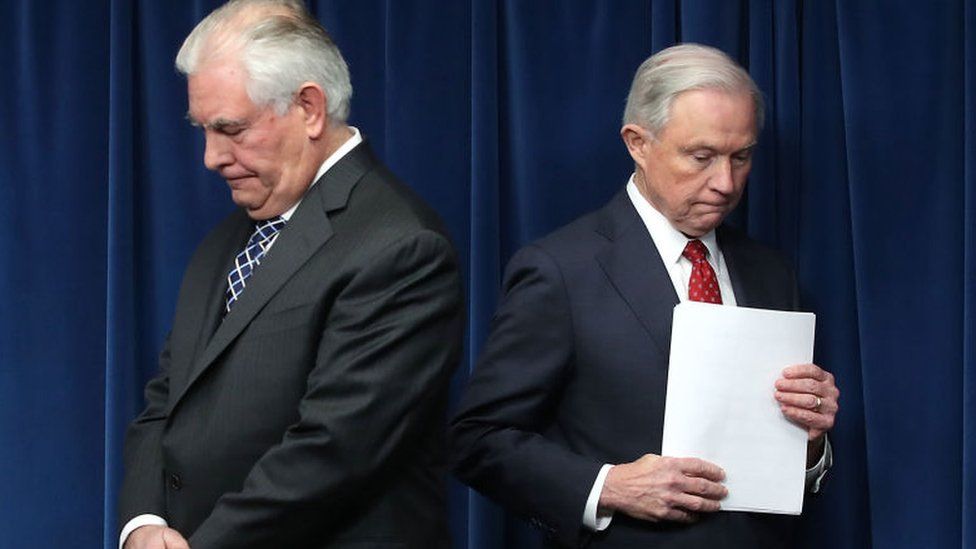 Rex Tilllerson and Jeff Sessions pause before a press briefing announcing the new travel ban.