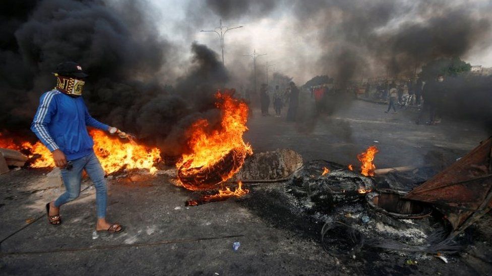 A demonstrator wearing a mask and walking above burning tyres in Basra, southern Iraq